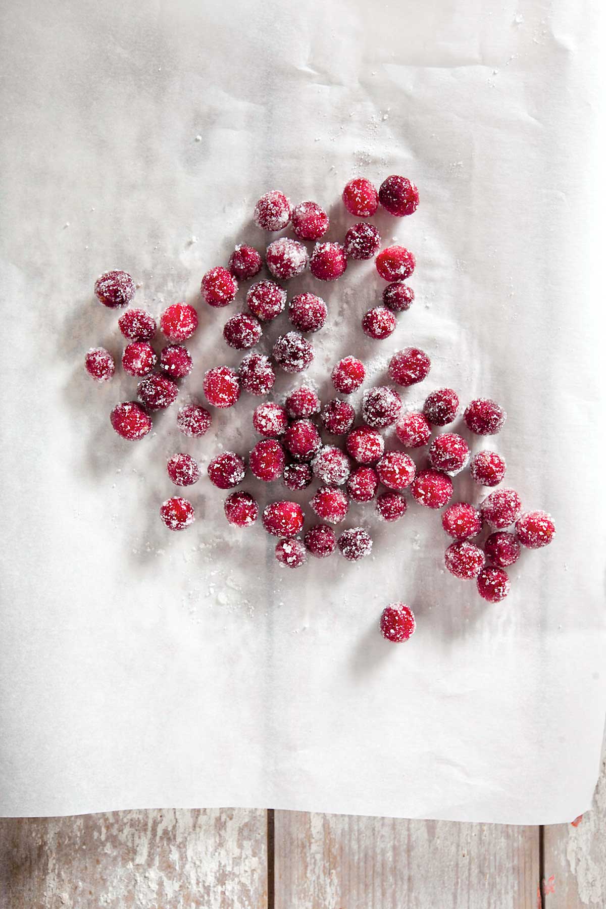 Several sugared cranberries scattered across a sheet of parchment.