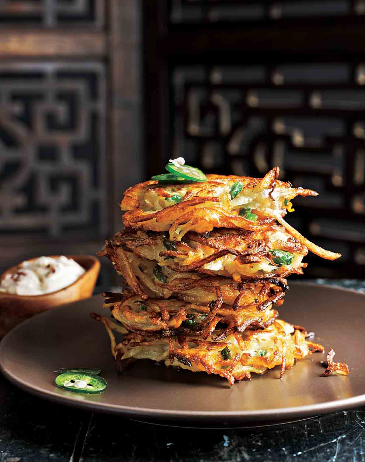 A stack of four cilantro-jalapeño latkes on a plate, with sliced jalapeño on top and sour cream on the side.