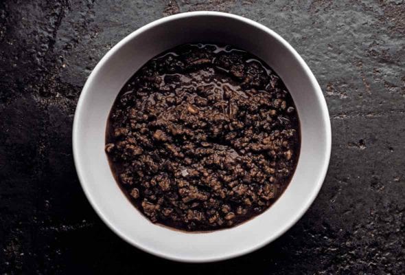 White bowl of dark beef chili with chocolate on a black slab