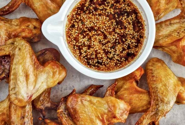 A pile of roasted chicken wings with a bowl of Korean dipping sauce with sesame seeds