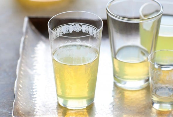 Several glasses partially filled with limoncello on a silver platter, with a bottle of limoncello in the background.