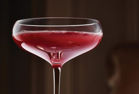 A coupe glass filled with blood orange prosecco cocktail on a small tray.