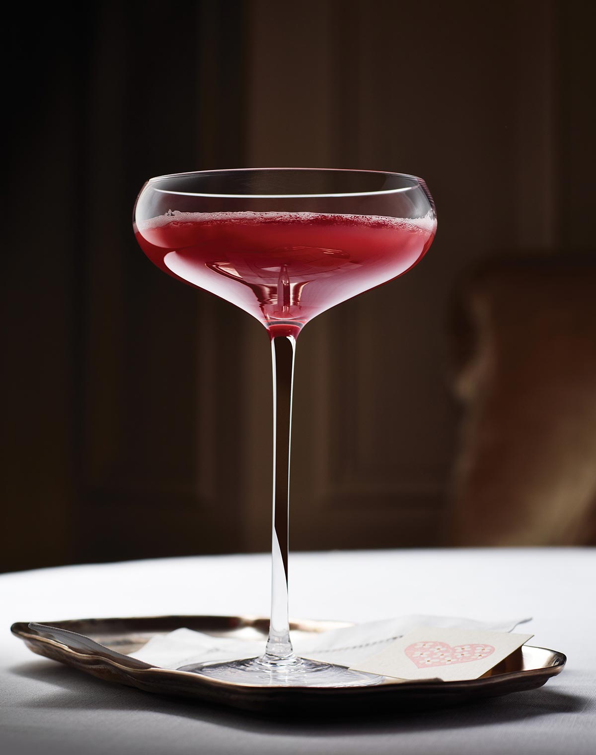 A coupe glass filled with blood orange prosecco cocktail on a small tray.