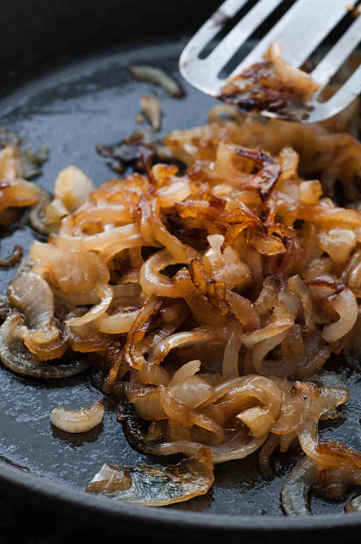 A skillet with caramelized onions and a spatula moving the onions.