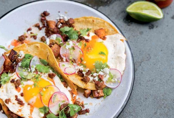 Two chorizo breakfast tacos with potatoes, eggs, radish, chorizo, cilantro, and Cotija cheese on a white plate.