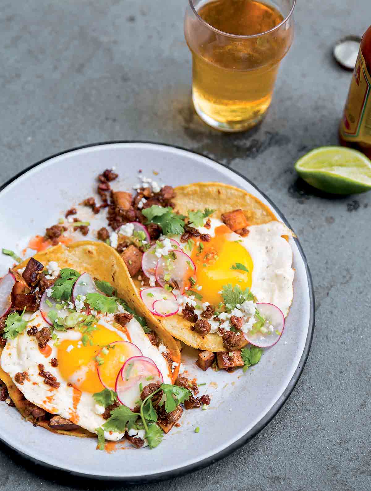Two chorizo breakfast tacos with potatoes, eggs, radish, chorizo, cilantro, and Cotija cheese on a white plate.