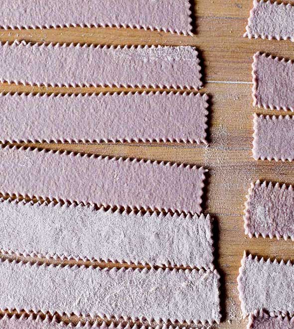 Long strips of fresh homemade red wine pasta laid on a wooden board