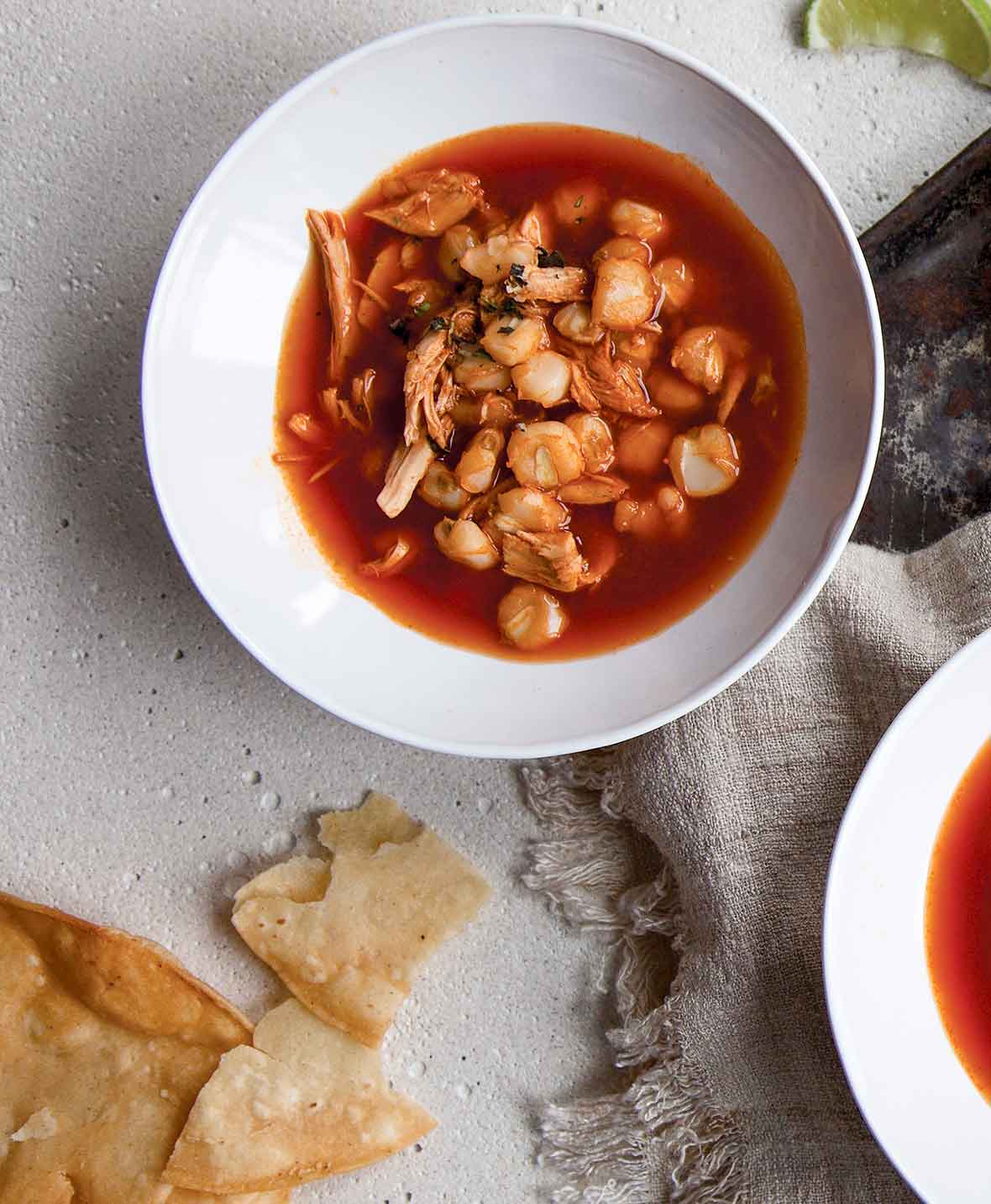 A white bowl of red pozole--a soup made with hominy, pork or chicken, and chiles