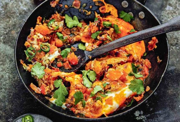 A skillet filled with spicy scrambled eggs with a wooden spoon inside.