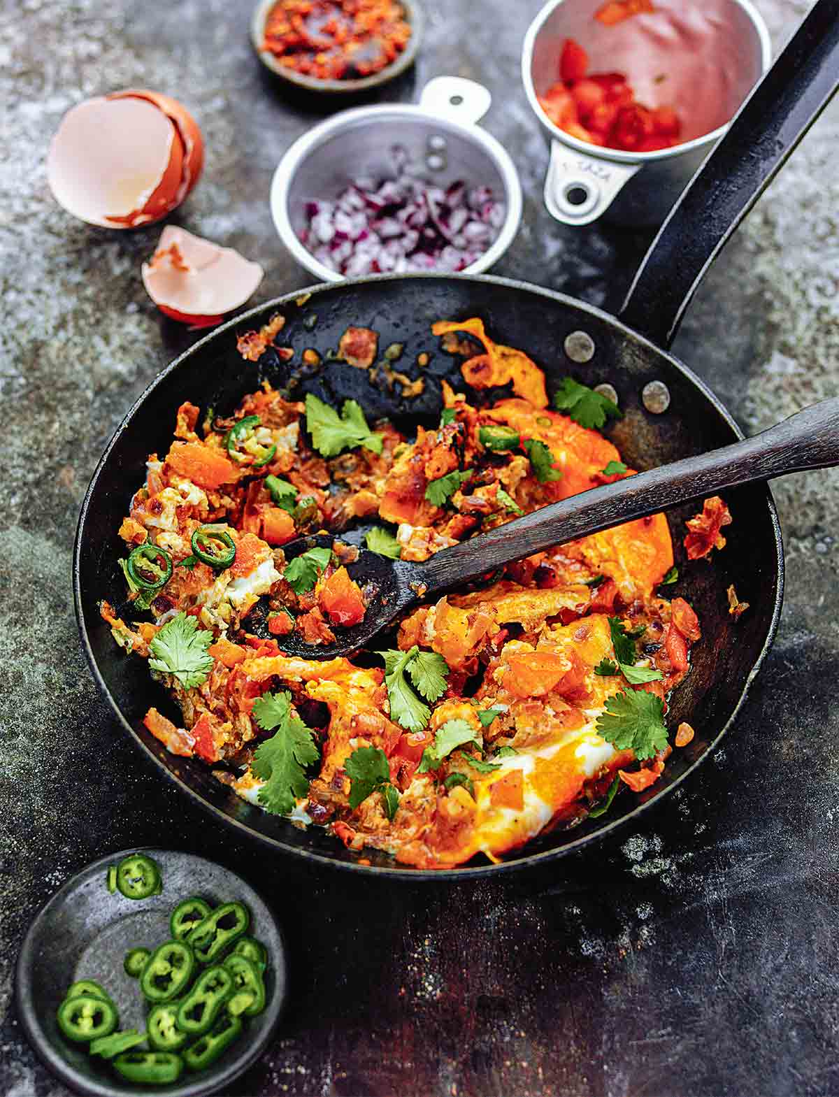 A skillet filled with spicy scrambled eggs with a wooden spoon inside.