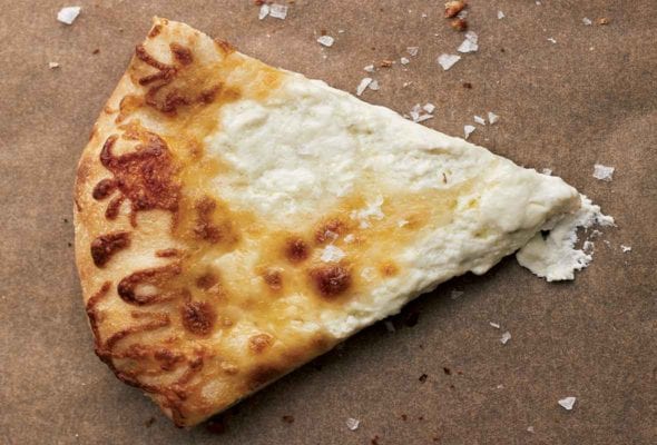 A slice of white pizza on a brown background with flaked salt scattered over and around it.