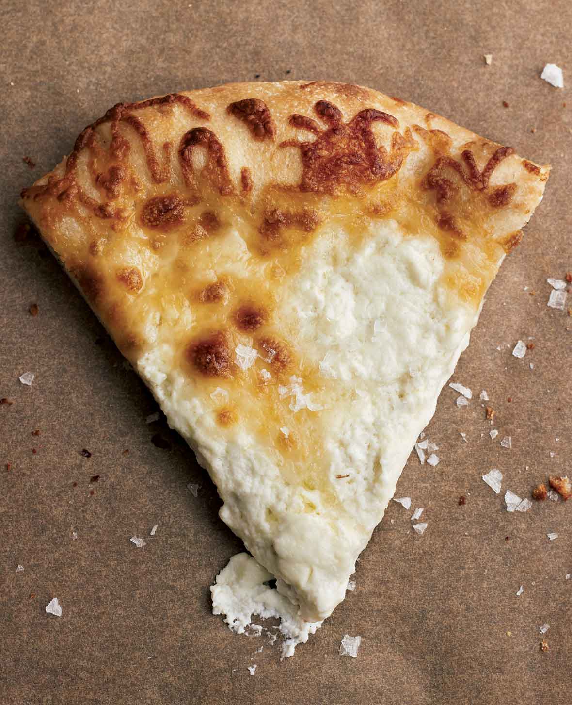 A slice of white pizza on a brown background with flaked salt scattered over and around it.
