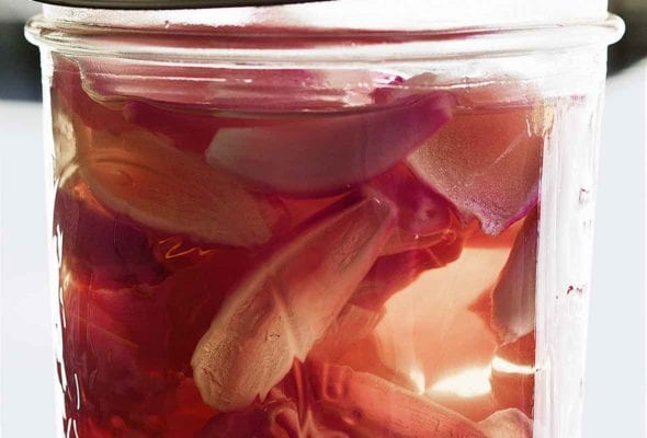 A jar filled with pickled shallots in pink pickling liquid.