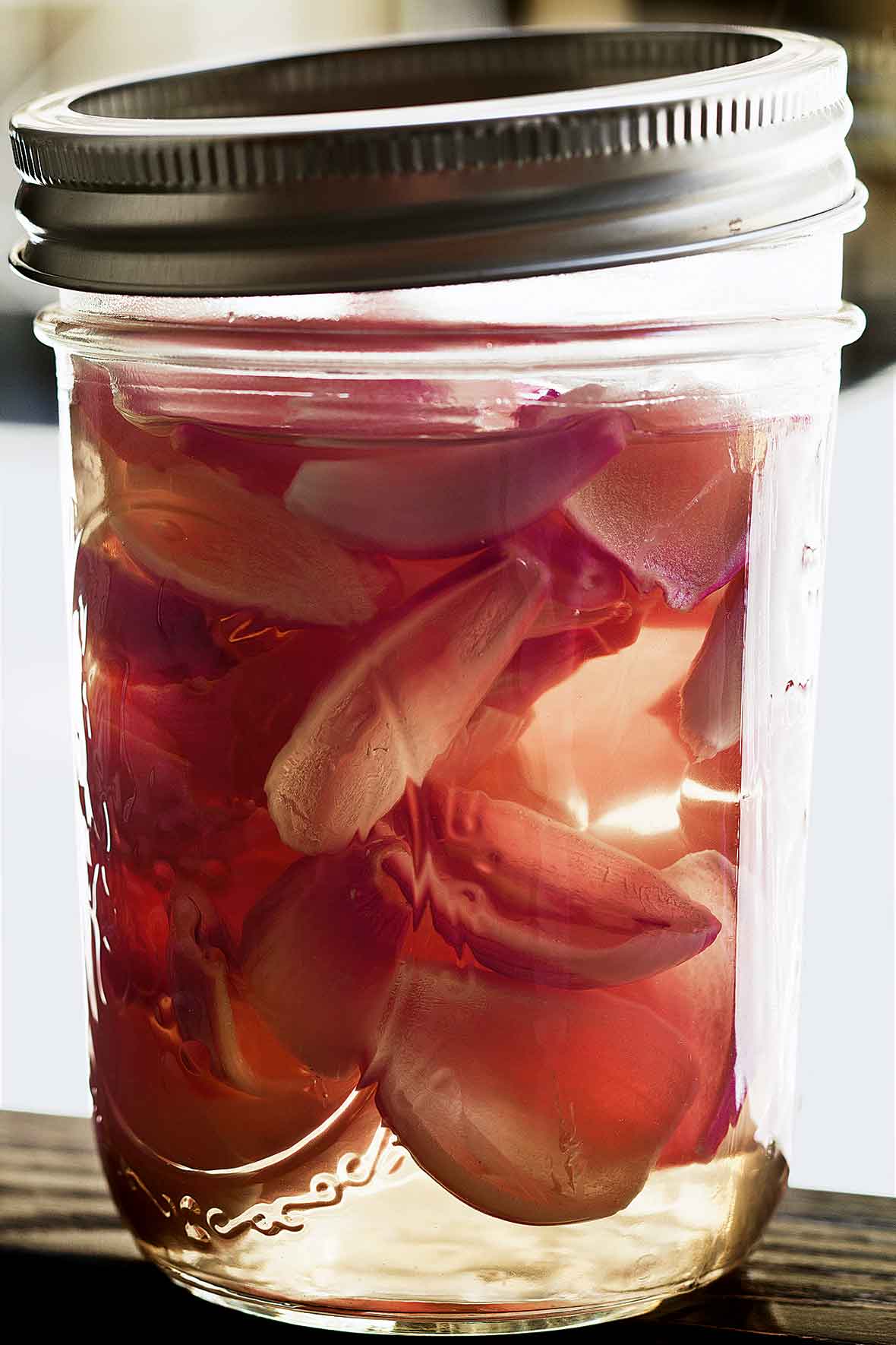 A jar filled with pickled shallots in pink pickling liquid.