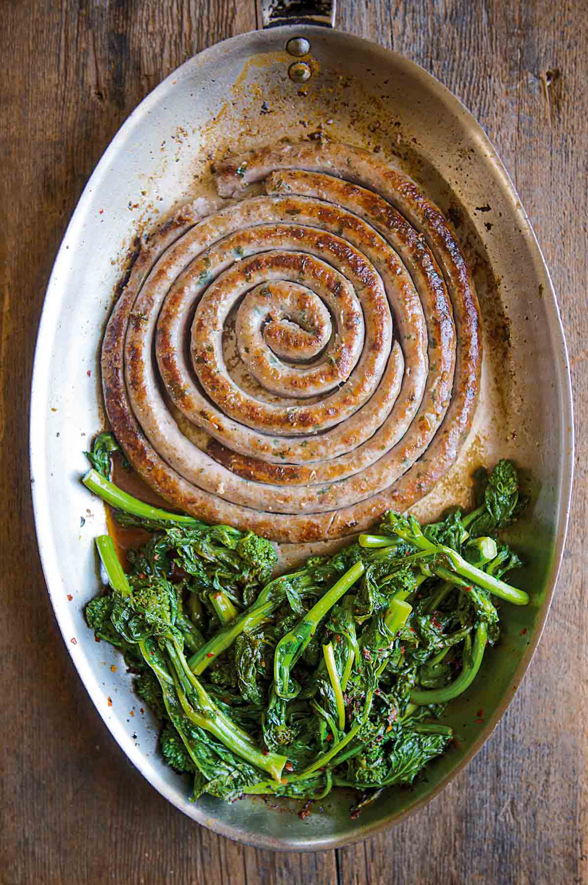 A large coil of Italian sausage and broccoli rabe in an oval skillet.