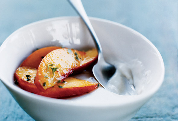 A white bowl filled with panna cotta with peaches on top and a spoon resting in the panna cotta.
