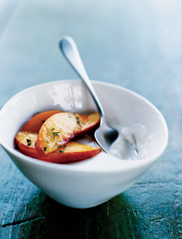 A white bowl filled with panna cotta with peaches on top and a spoon resting in the panna cotta.