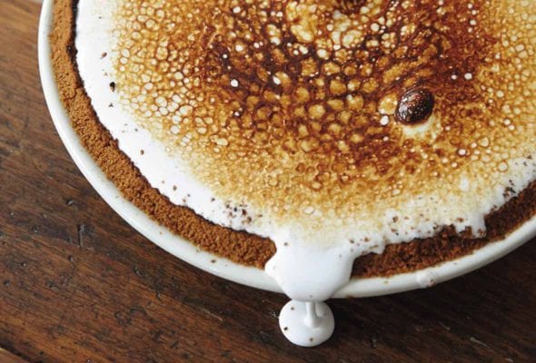 A whole s'mores pie with a bit of the marshmallow layer dripping down the side on a wooden surface.