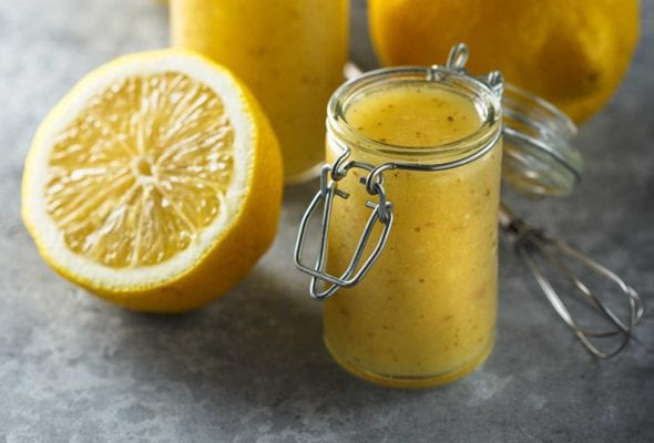 Two jars of lemon vinaigrette, two lemon halves, and a wire whisk.