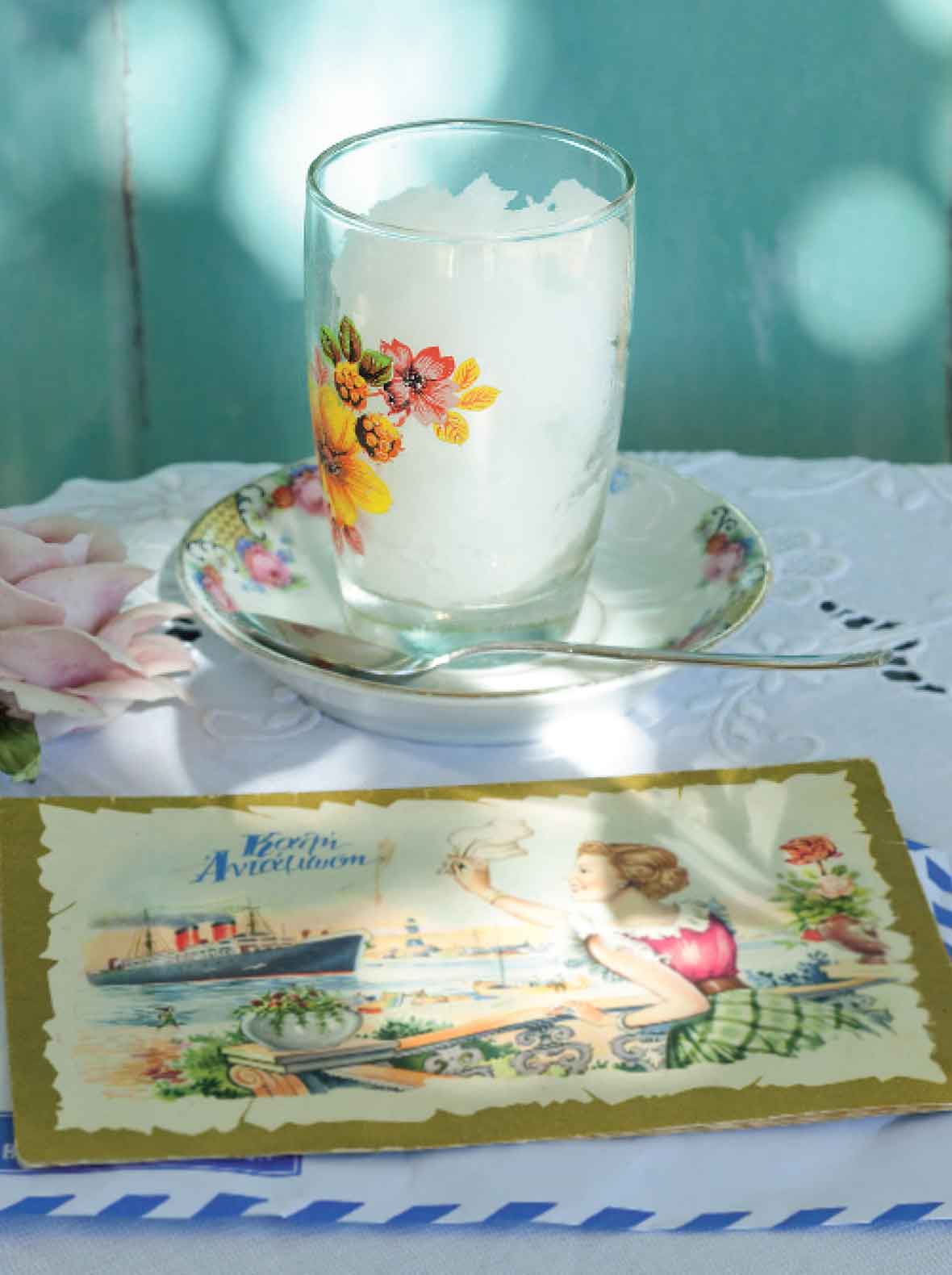 A glass filled with ouzo sorbet in a small china dish with a spoon resting beside it.