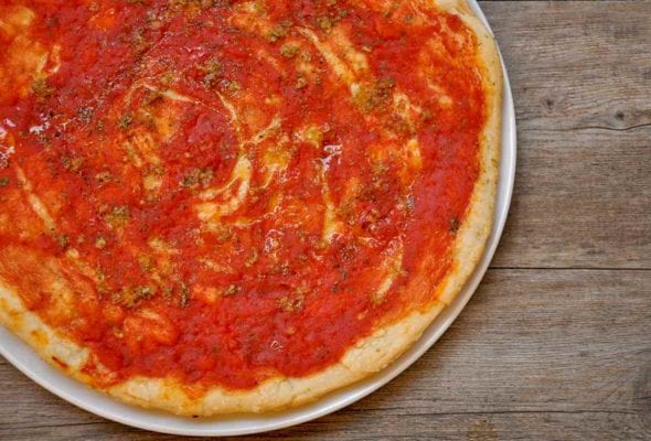A tomato pizza, called pizza marinara, on a plate with oregano and garlic