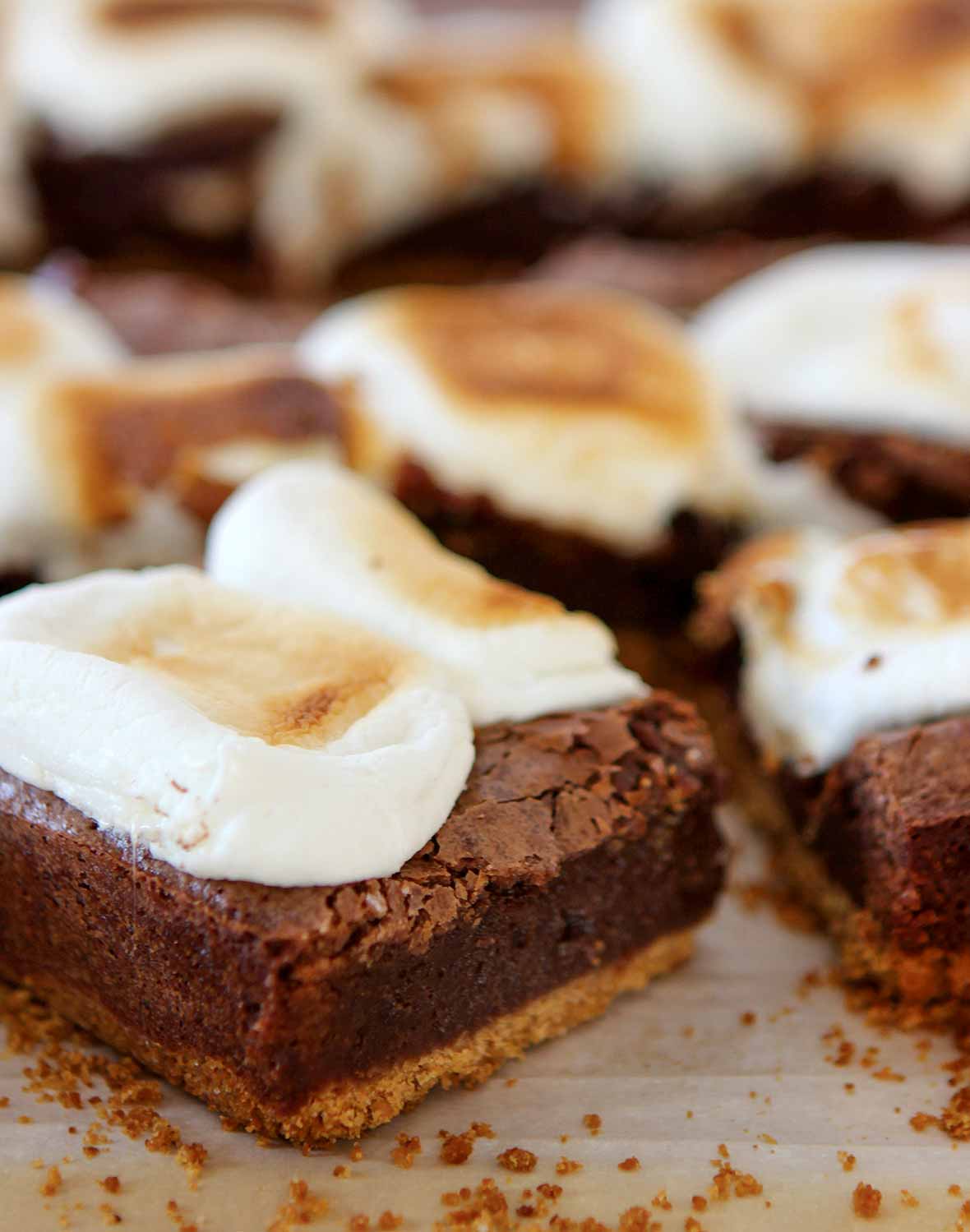 Several bars of cut s'mores brownies made with graham crust, fudgy layer and topped with marshmallow on a piece of parchment.