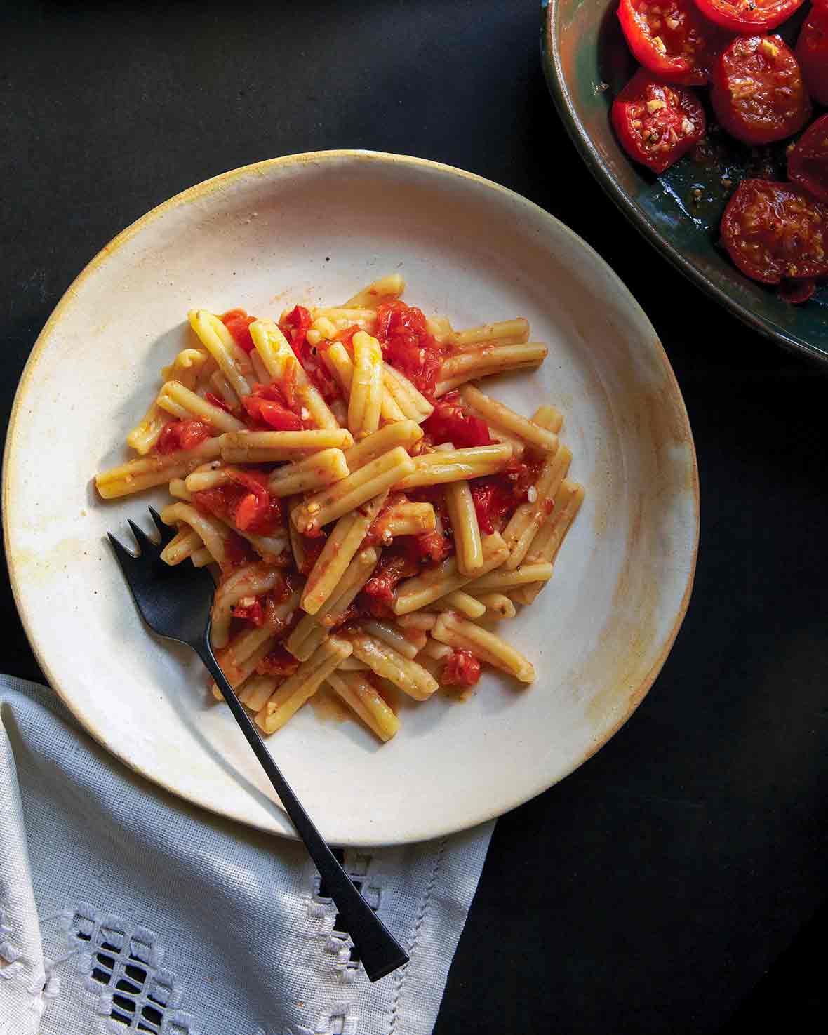 A white plate with cavatelli past topped with a roasted tomato sauce, fork on the side
