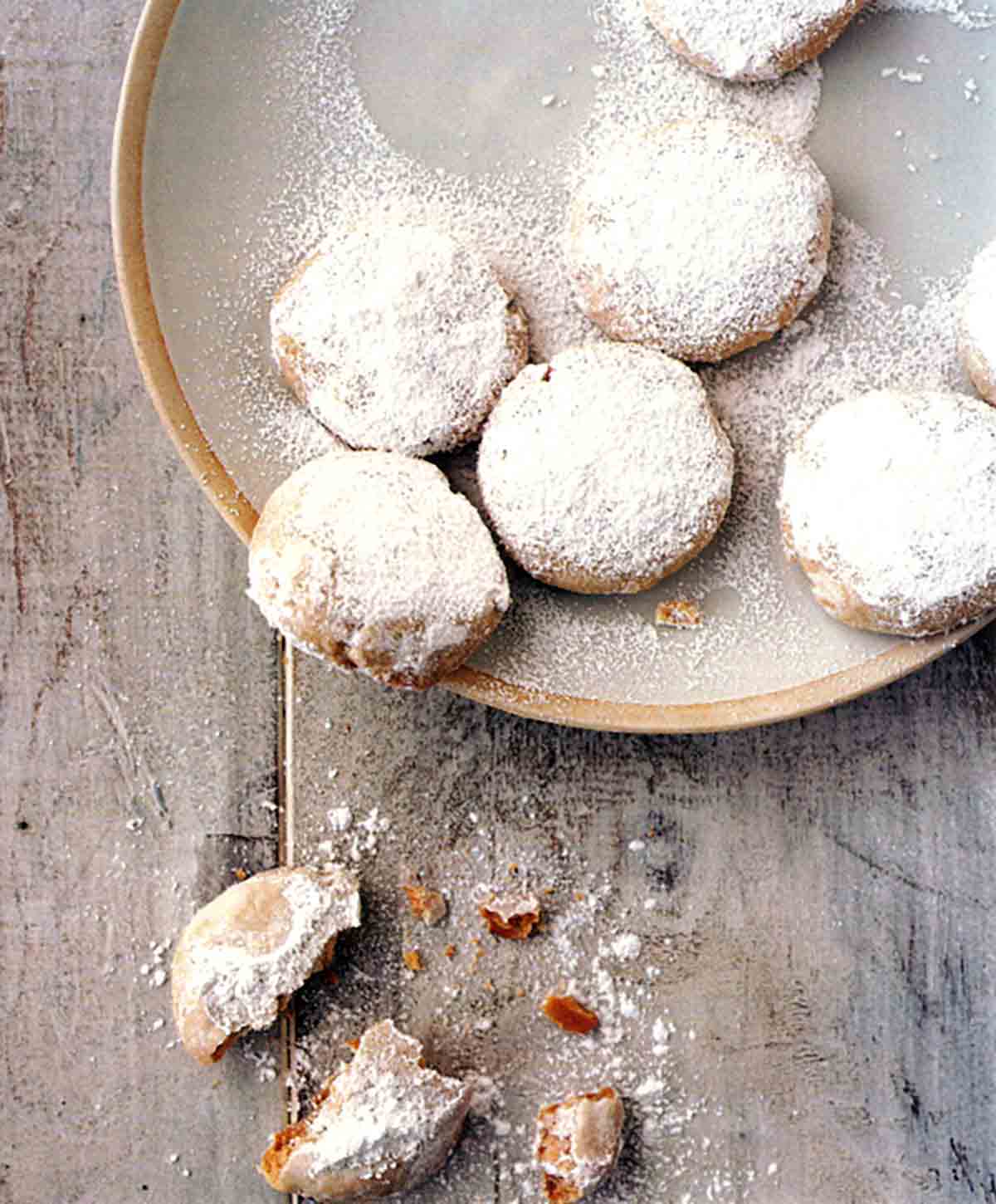 A bowl of cardamom and cashew cookies with one broken cookie beside the bowl.