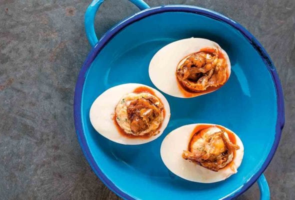 A blue pot containing three deviled eggs with roast chicken skin.