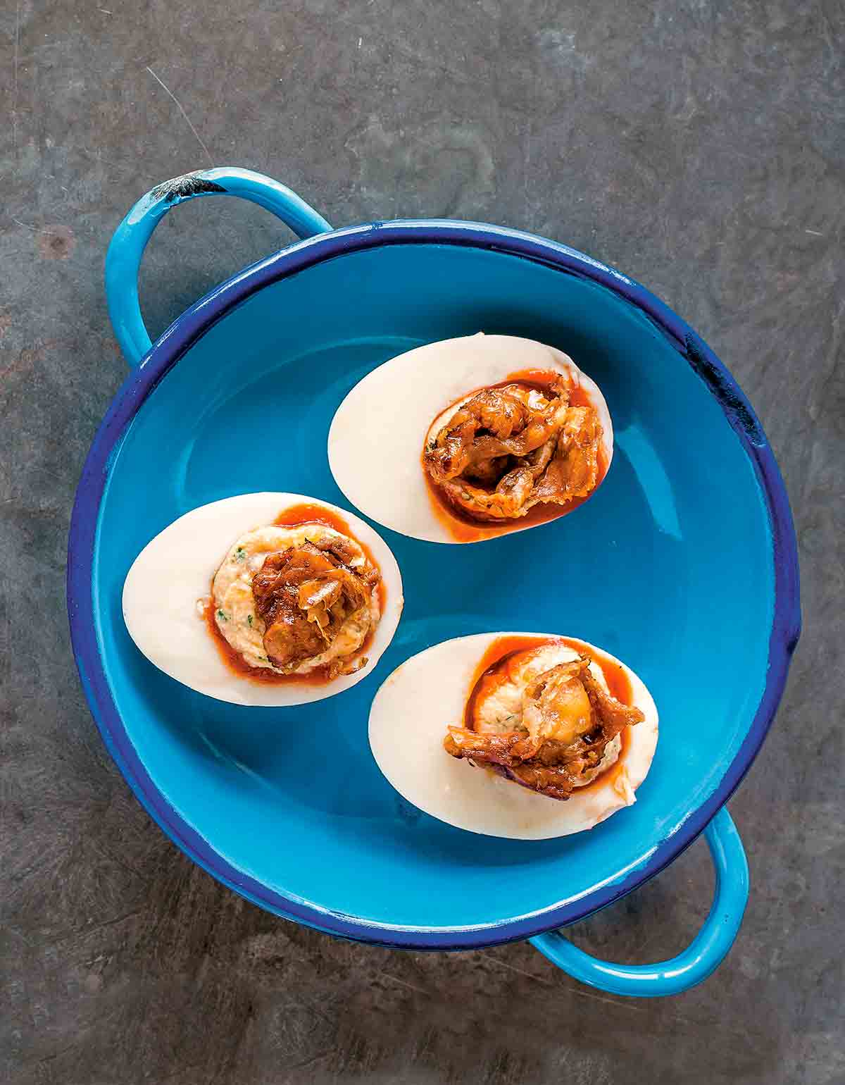 A blue pot containing three deviled eggs with roast chicken skin.