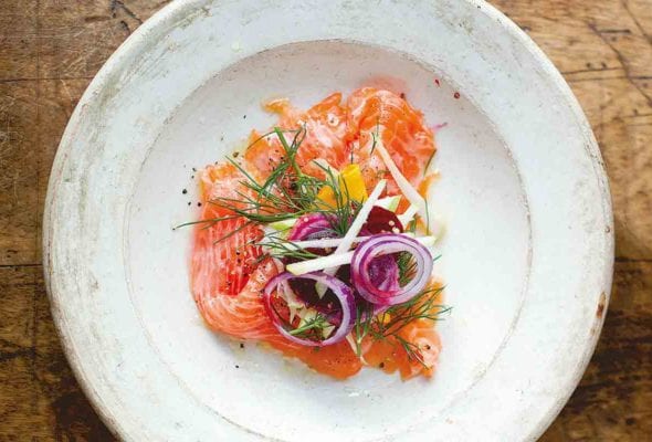 A white plate with salmon, fennel, and apple salad topped with red onion and dill.