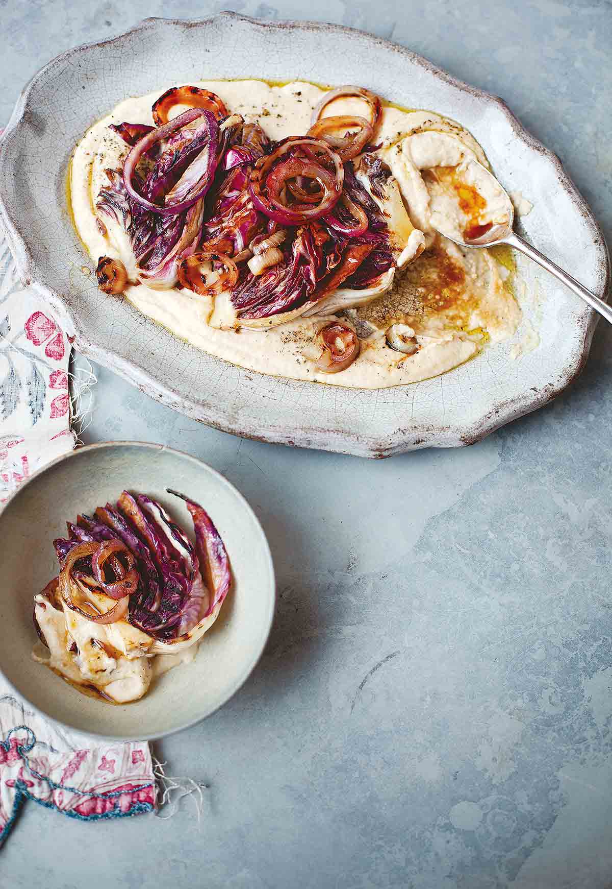 An oval platter filled with white bean puree, radicchio, and red onions with a spoon resting in it and a serving in a bowl beside.
