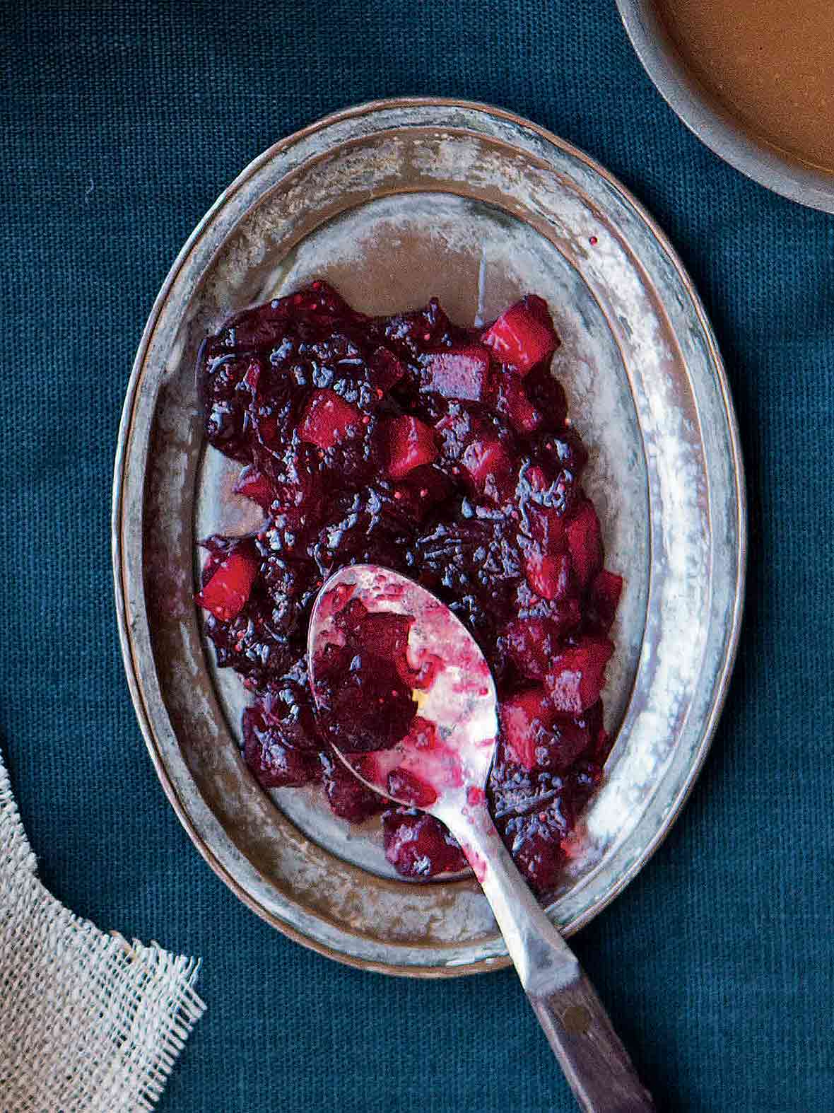 A pewter platter with chunky red apple cranberry sauce with a serving spoon