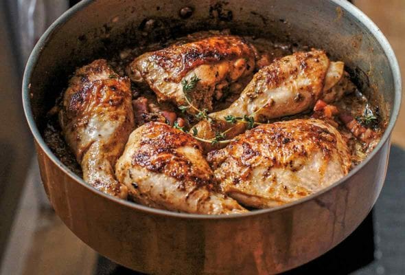 A skillet with browned chicken pieces cooked with mustard, wine, and thyme