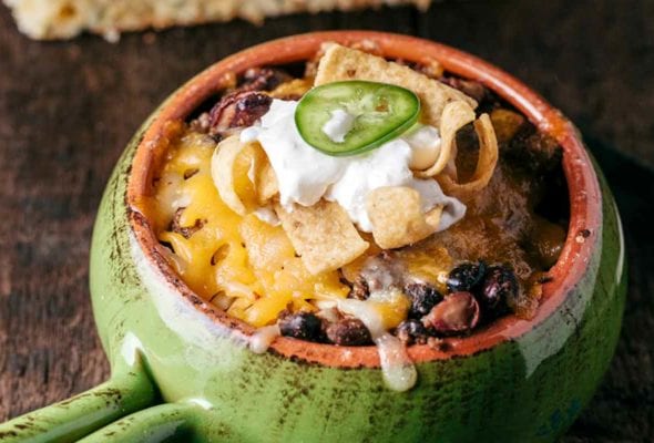Frito pie in a green enamel bowl with a handle with two pieces of jalapeno bread in the background.