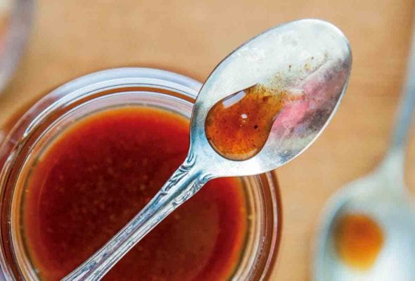 A jar of pumpkin spice syrup with a spoon resting on top and two spoons beside the jar.