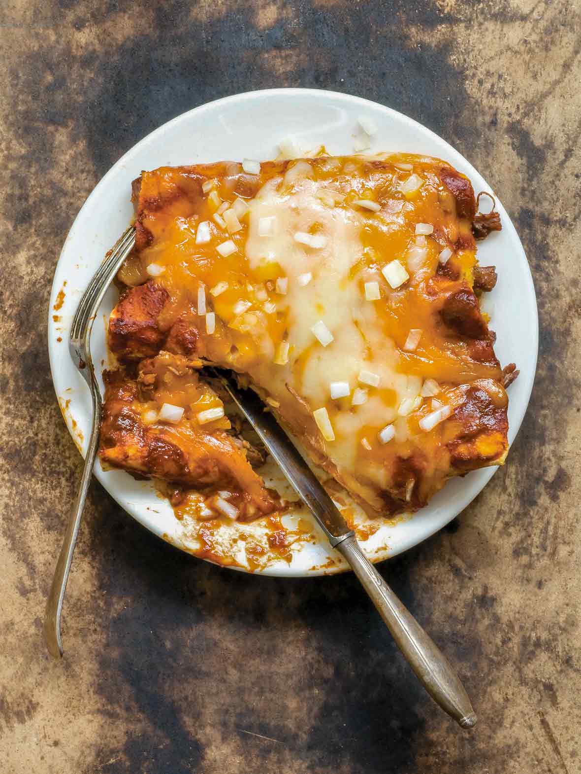 Plate of beef, tortillas, and red sauce, topped with cheese and diced onion, on a stone