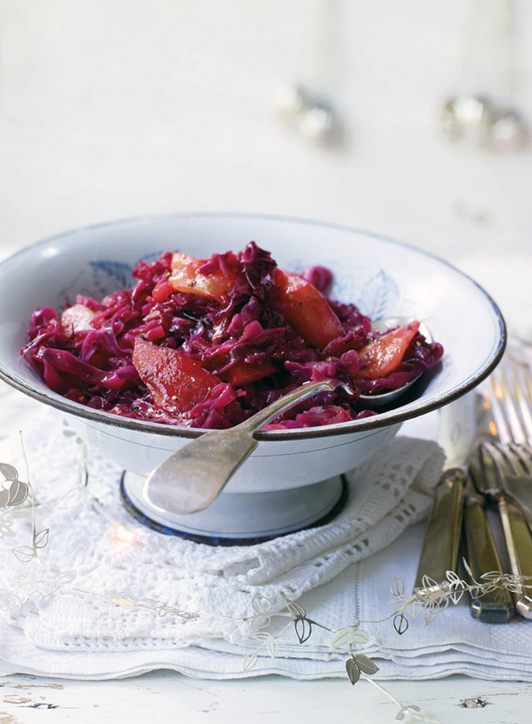 A white bowl filled with spiced red cabbage set on white linens with a spoon resting inside.