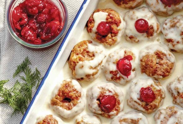 A white tray filled with Swedish meatballs--a combination of veal, pork, and beef--filled with cranberry sauce and topped with a white cream sauce
