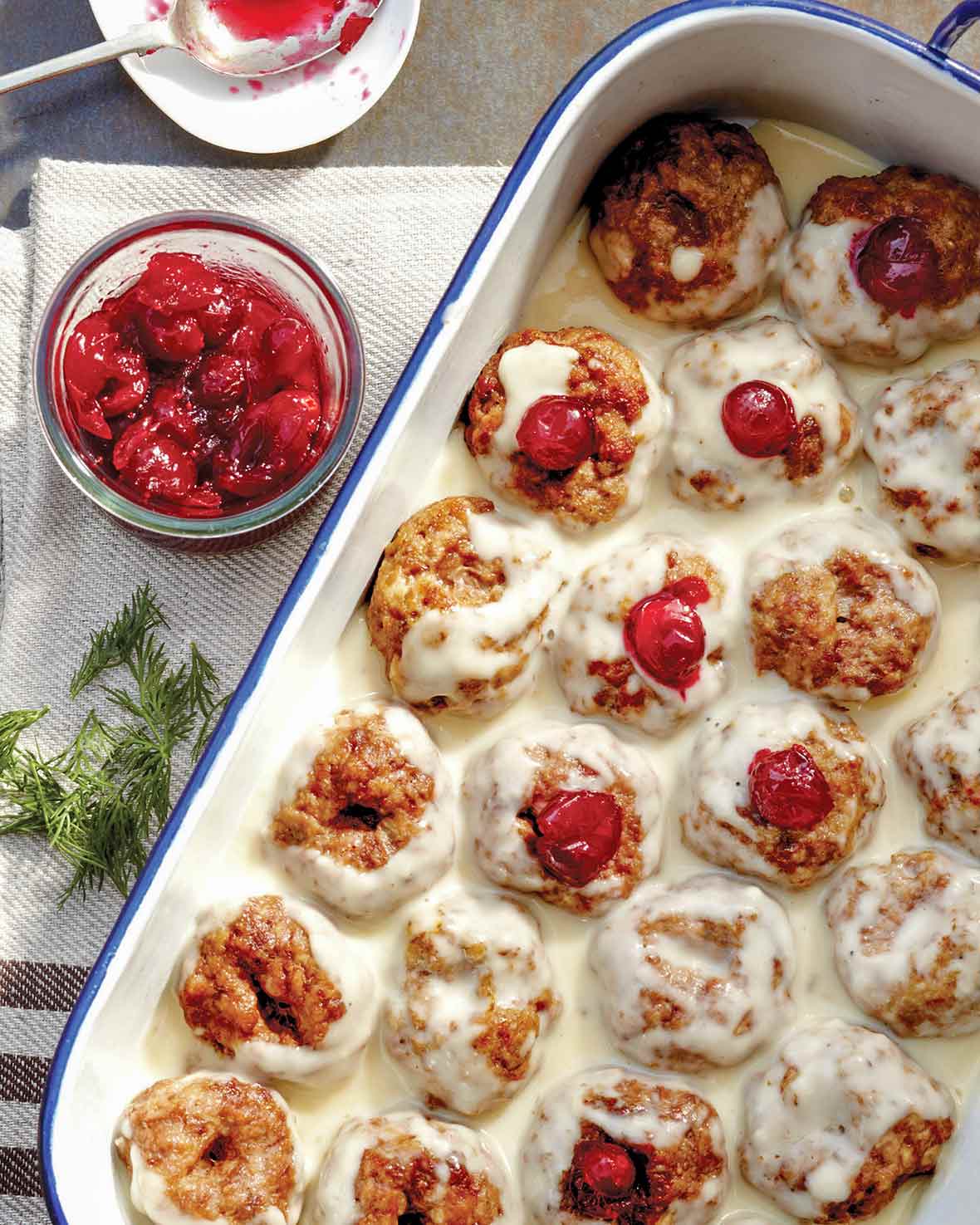 A white tray filled with Swedish meatballs--a combination of veal, pork, and beef--filled with cranberry sauce and topped with a white cream sauce