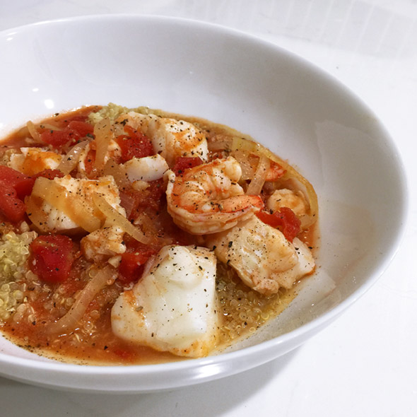A white bowl filled with cod and shrimp stew with quinoa.