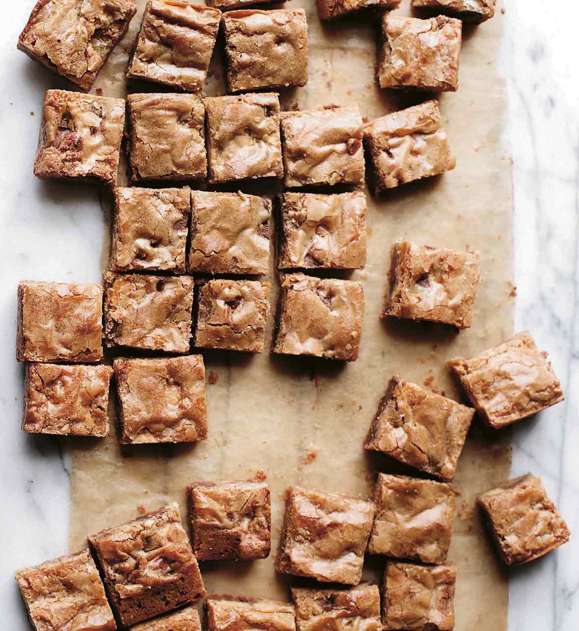 Squares of blondies with chocolate chips on parchment paper on a marble slab