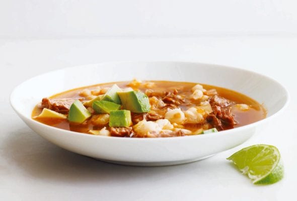 A white bowl filled with quick posole topped with avocado with a lime wedge on the side.