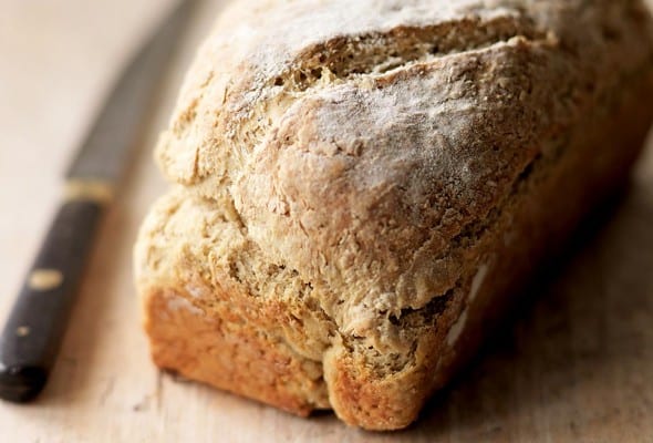 An unsliced loaf of brown soda bread with a knife resting beside it