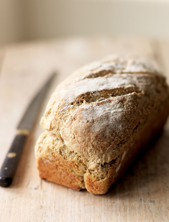 An unsliced loaf of brown soda bread with a knife resting beside it