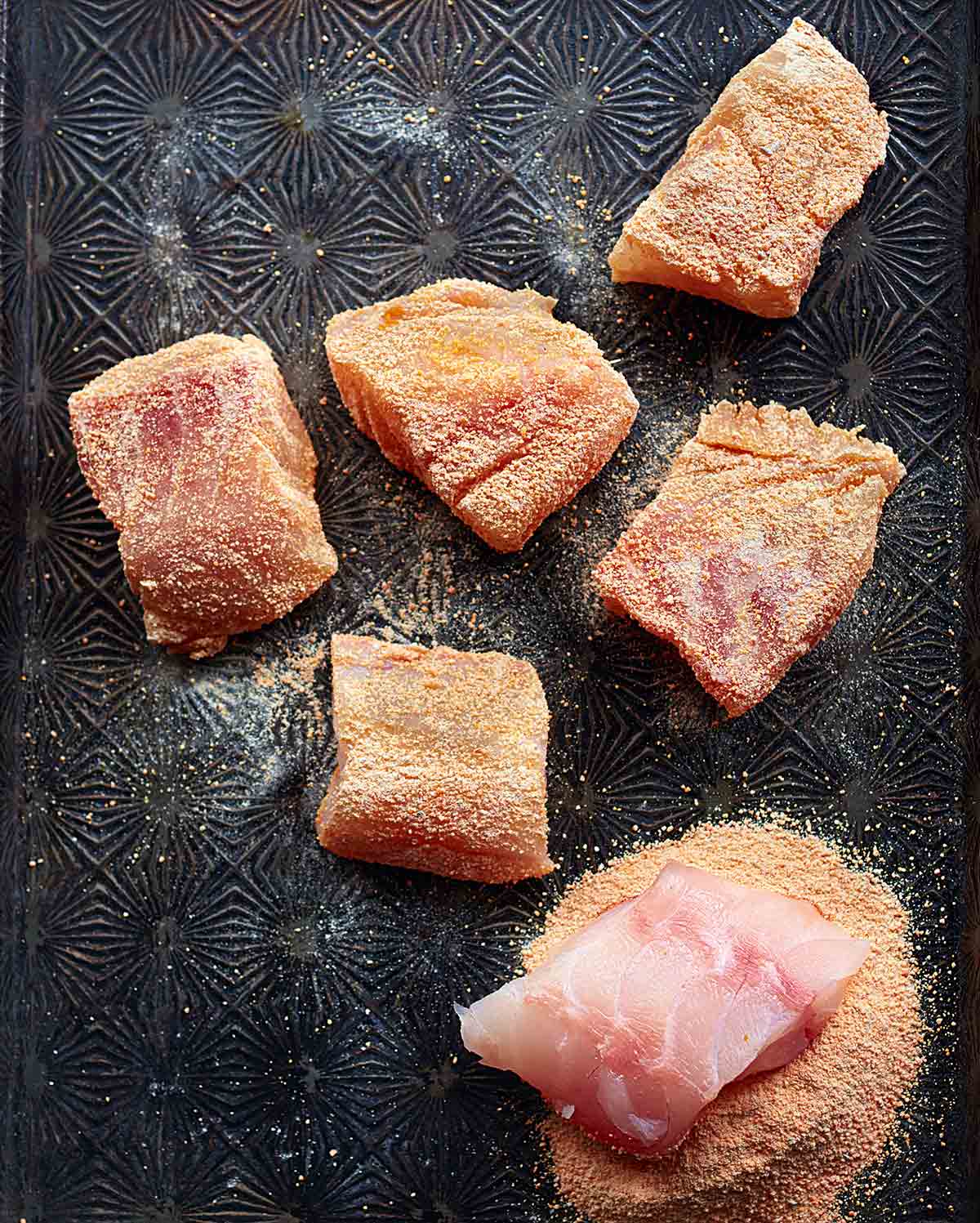 Six pieces of red lentil-crusted fish on a metal surface.