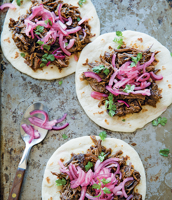 Three ancho short rib tacos on flour tortillas, topped with pickled red onion and cilantro.