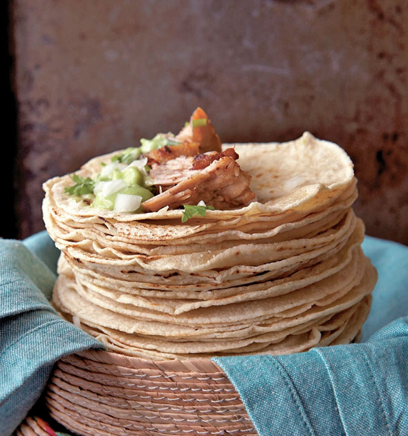A stack of flour tortillas topped with pork for carnitas tacos.