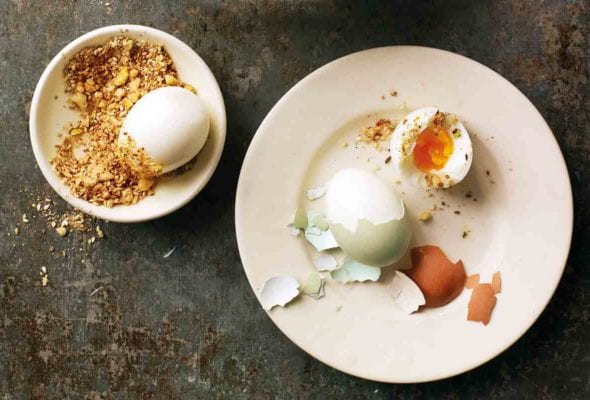 Two hard-boiled eggs with dukkah in a bowl next to it.