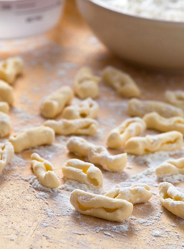 Pieces of uncooked homemade cavatelli on a floured surface.